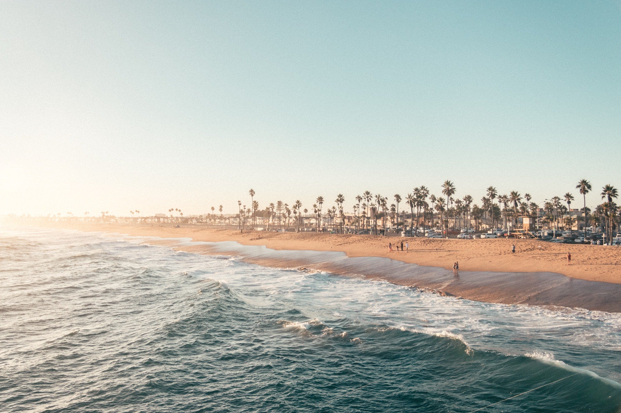 California coastline with clear blue sky, waves, sand, palm trees, and bright sun perfect for e-bikes