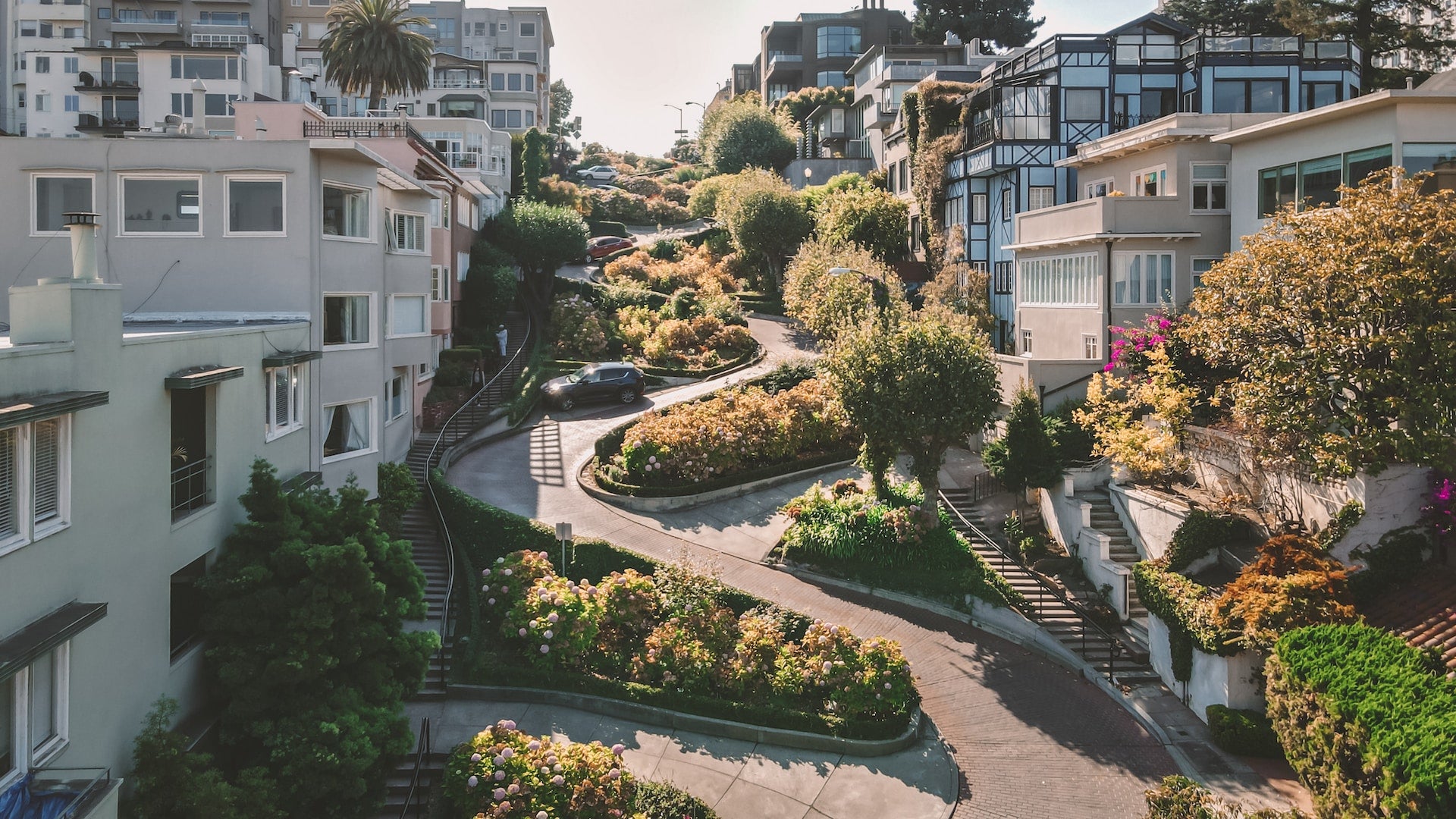 A sunny view looking up Lombard Street in San Francisco California; the winding street is perfect for e-bikes, lined with bushes and trees along with paths and staircases in between the buildings