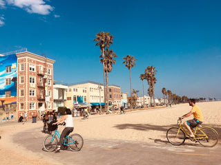 Bicyclists along a paved e-bike path that winds around the sand near buildings in Venice Beach