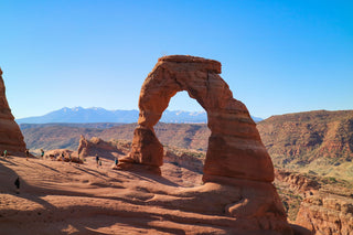 Clear blue sky and orange landscape at Arches National Park featuring Delicate Arch; some hikers can be seen on the terrain