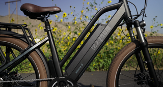 Close-up of a black Magnum electric bike with brown tires in front of yellow wildflowers
