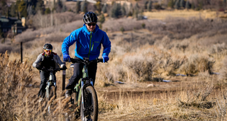Two riders in gloves and jackets power up a dry desert hill on Peak T7 mountain e-bikes